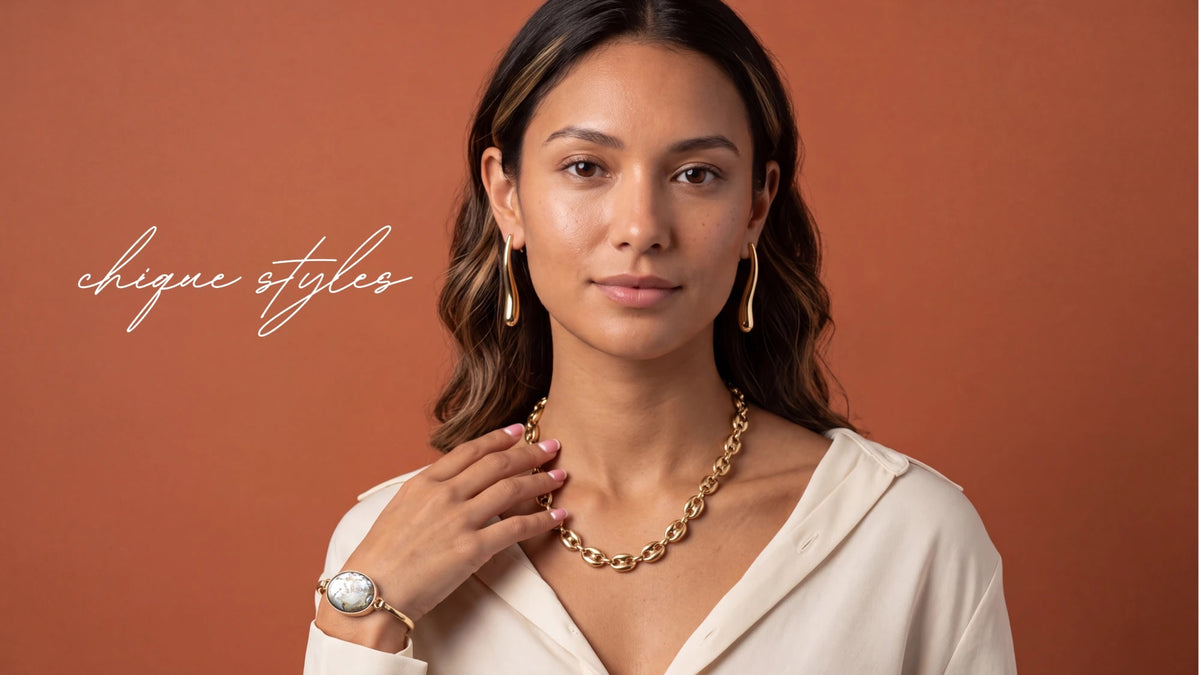 Model wearing a gold chain-link necklace, gold hoop earrings and a bangle watch